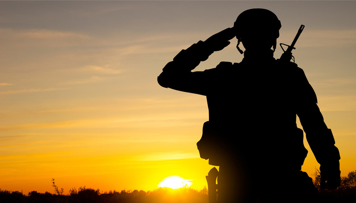 Silhouette of a soldier saluting against a sky with a setting sun.