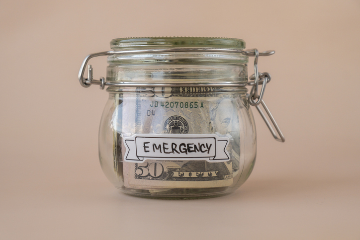 A glass jar with a secure lid labeled "EMERGENCY" contains a folded fifty-dollar bill, symbolizing savings for unexpected expenses.